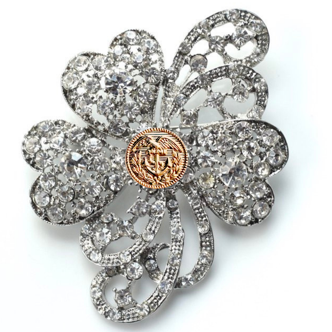 Decorative brooch with crystal-like stones and a central gold emblem on a white background