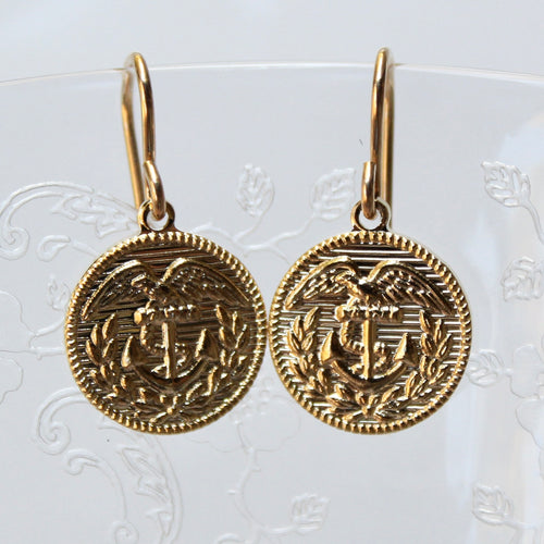 Gold coin-shaped earrings with anchor design on a textured white background