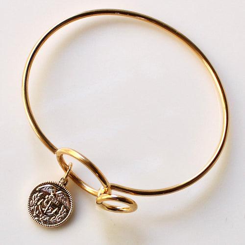 Gold bangle with a small round charm on a light gray background