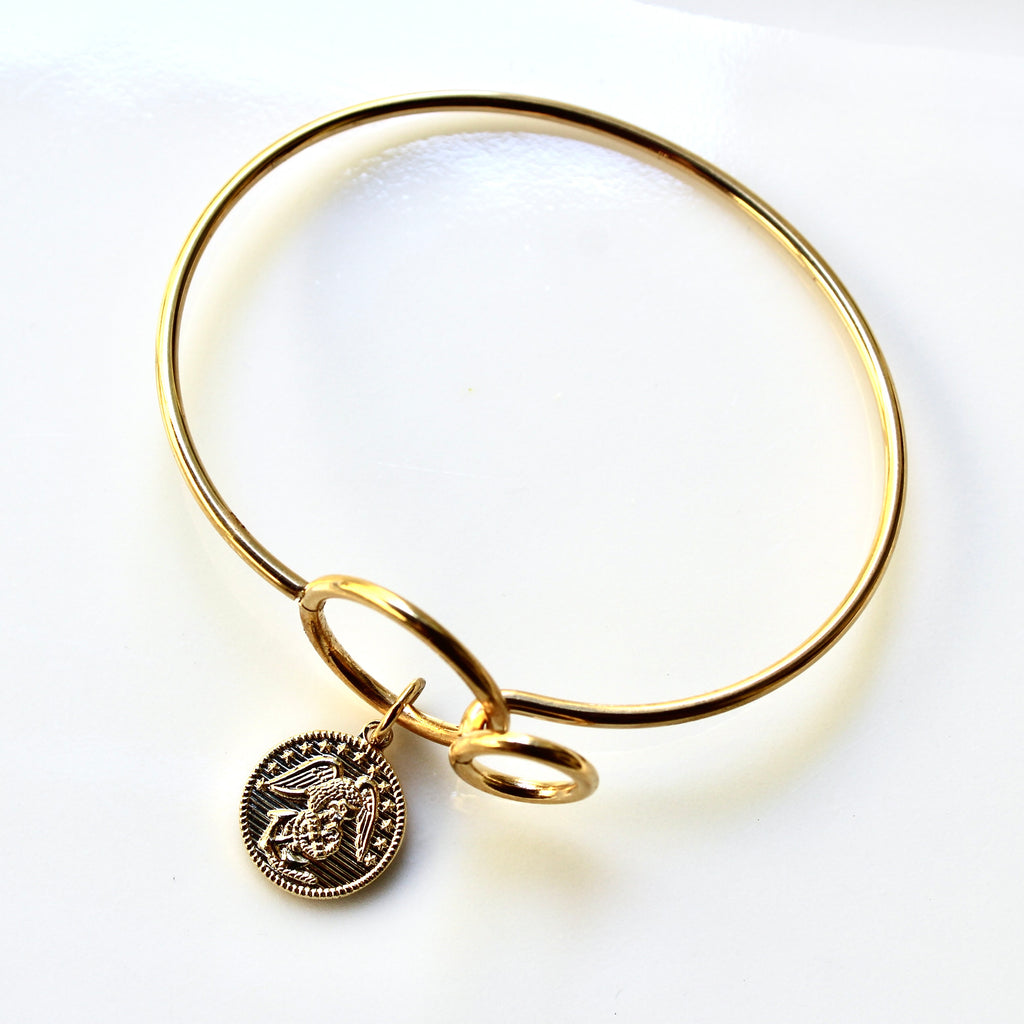Gold bangle with a coin charm on a white background