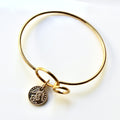 Gold bangle with a coin charm on a white background