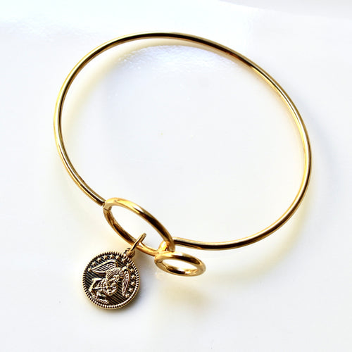 Gold bangle with a coin charm on a white background