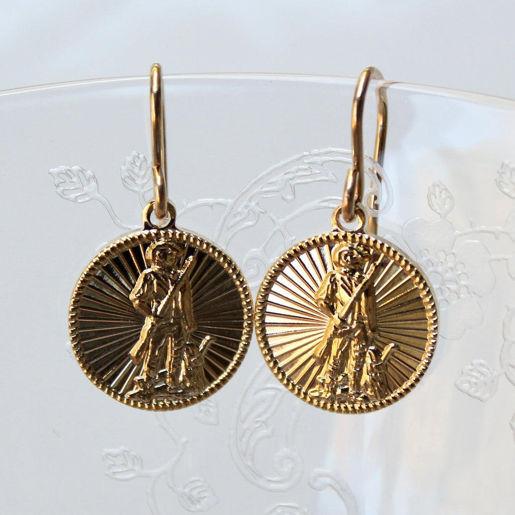 Gold coin-shaped earrings with religious design on a white background