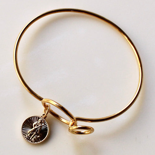 Gold bangle with a small round charm on a light background
