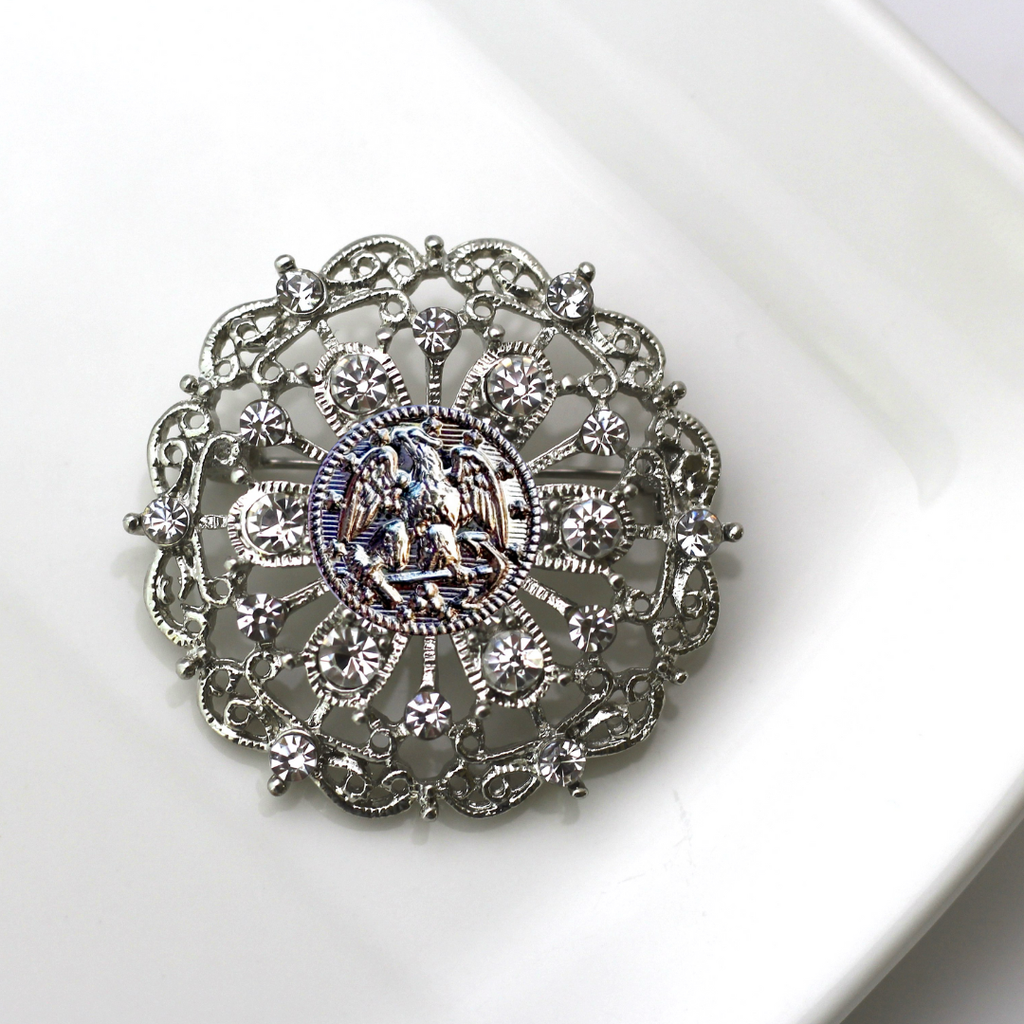 Decorative brooch with intricate design and central Navy inspired insginia on a white background