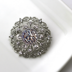 Decorative brooch with intricate design and central Navy inspired insginia on a white background