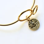 Gold bracelet with a coin charm on a white background
