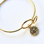 Gold bracelet with a circular charm on a white background