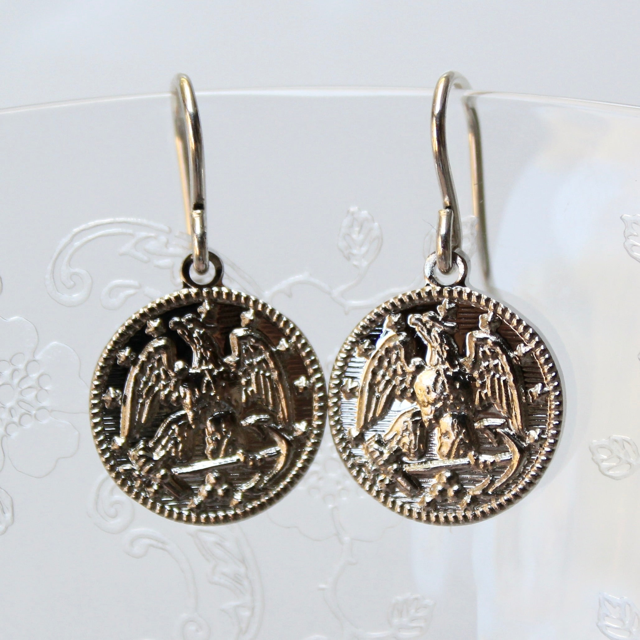 Pair of coin-shaped earrings with an eagle design on a white background