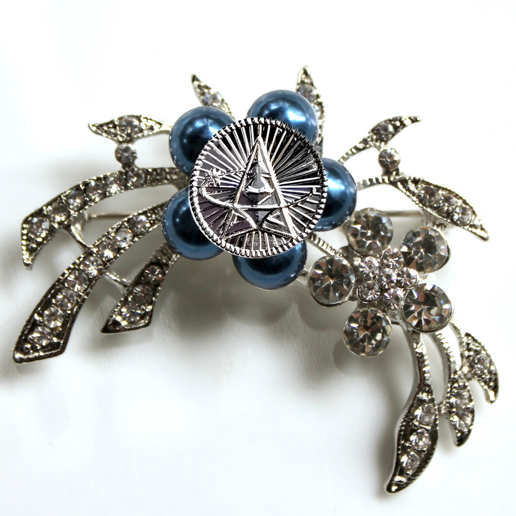 Decorative brooch with blue pearls and silver leaves on a white background