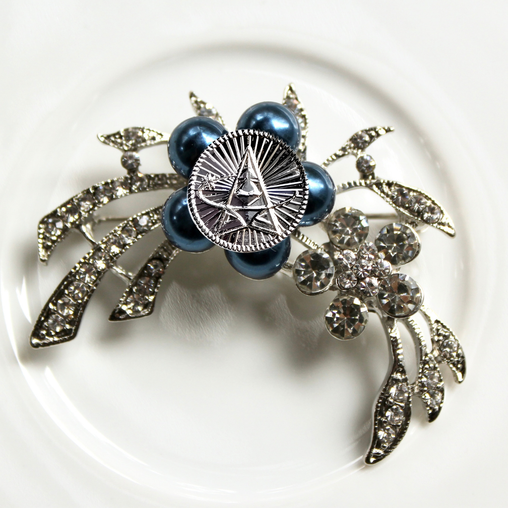 Decorative brooch with blue pearls and silver leaves on a white background