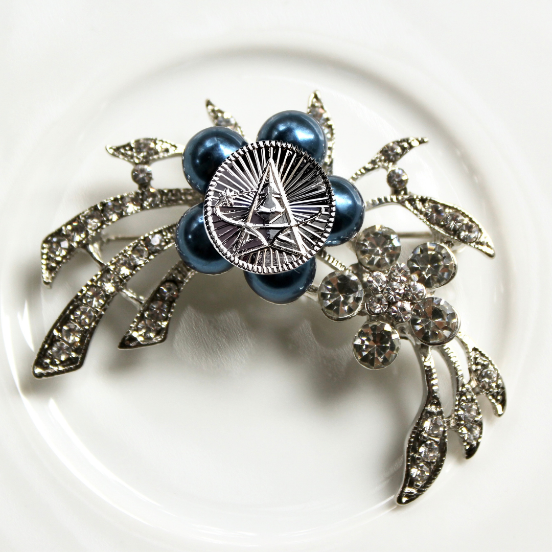 Decorative brooch with blue pearls and silver leaves on a white background