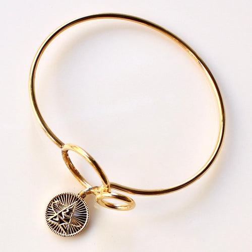 Gold bracelet with a circular charm on a white background