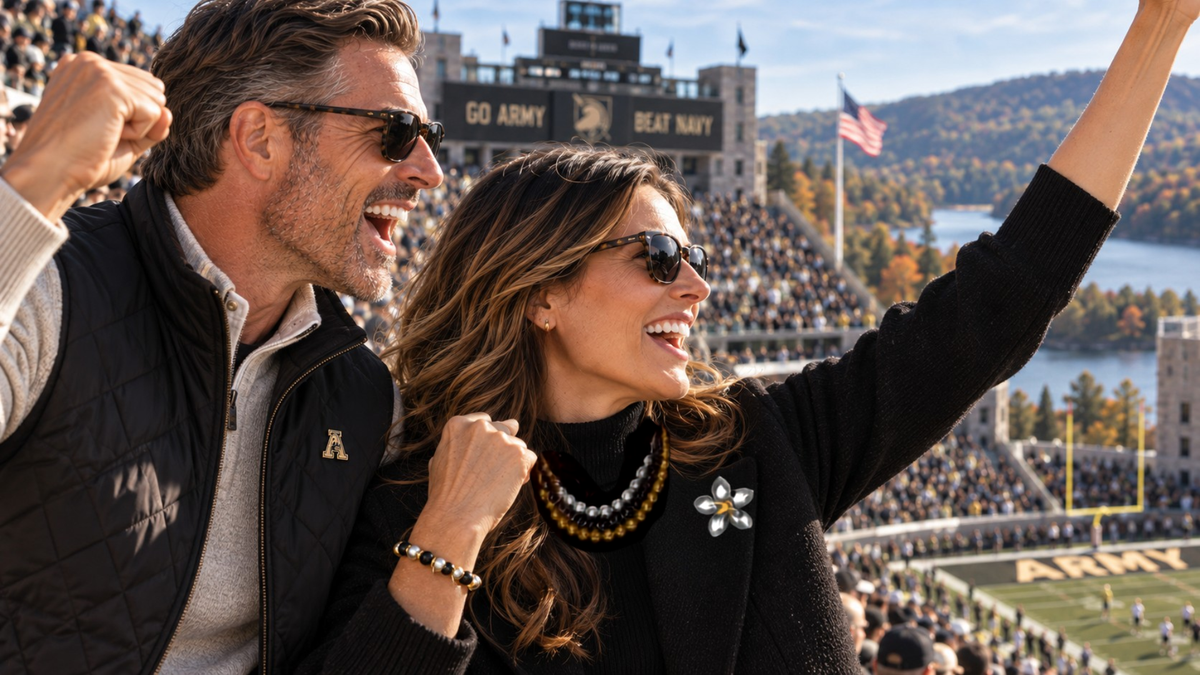 A man and a woman wearing black quilted jackets and sunglasses cheer excitedly at a football game, with a stadium crowd and 'Go Army, Beat Navy' scoreboard in the background.