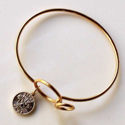 Gold bangle with a charm on a light background