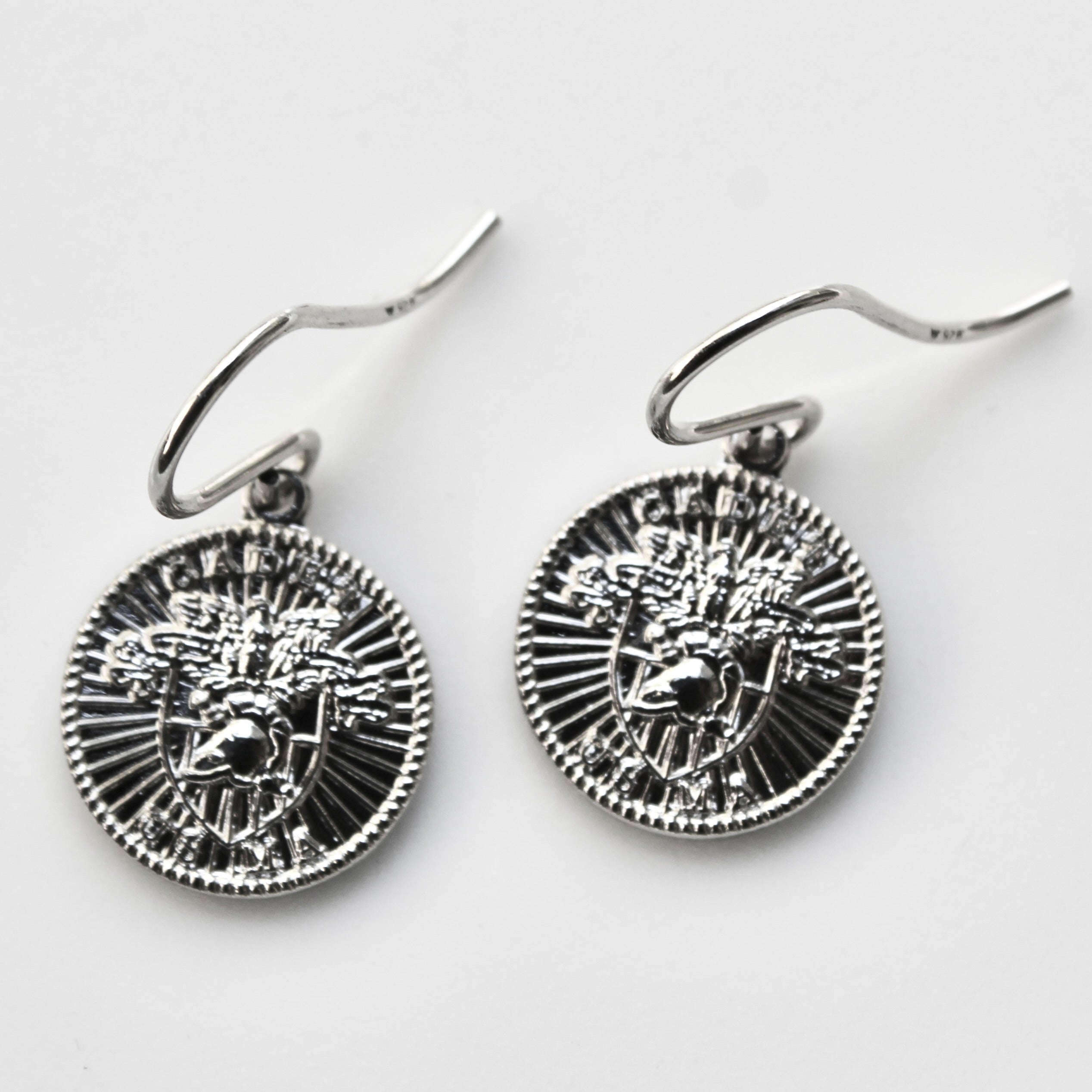 Pair of silver earrings with intricate designs on a light gray background