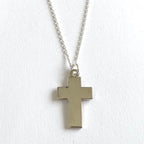A charm in the shape of a cross with a silver-tone steel chain against a white background.
