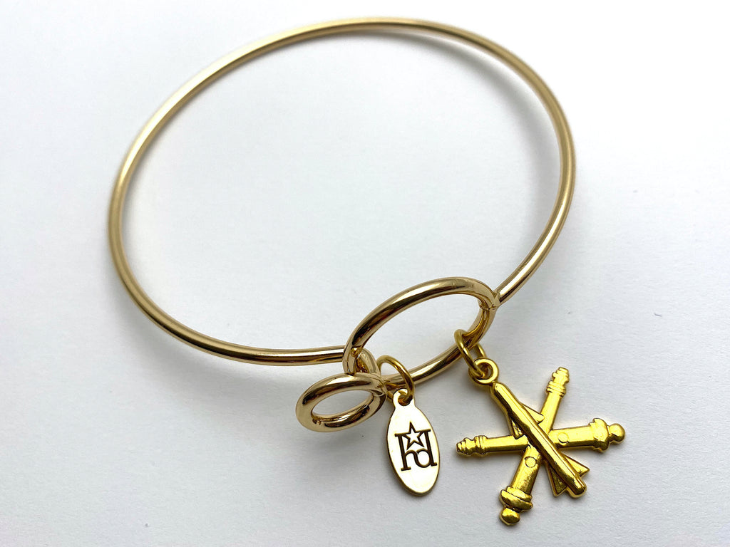 A gold-colored wire bracelet with the US Army Air Defense Artillery branch insignia.