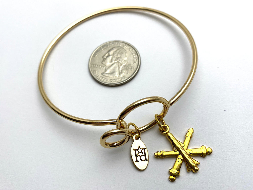 A gold-colored wire bracelet with the US Army Air Defense Artillery branch insignia.