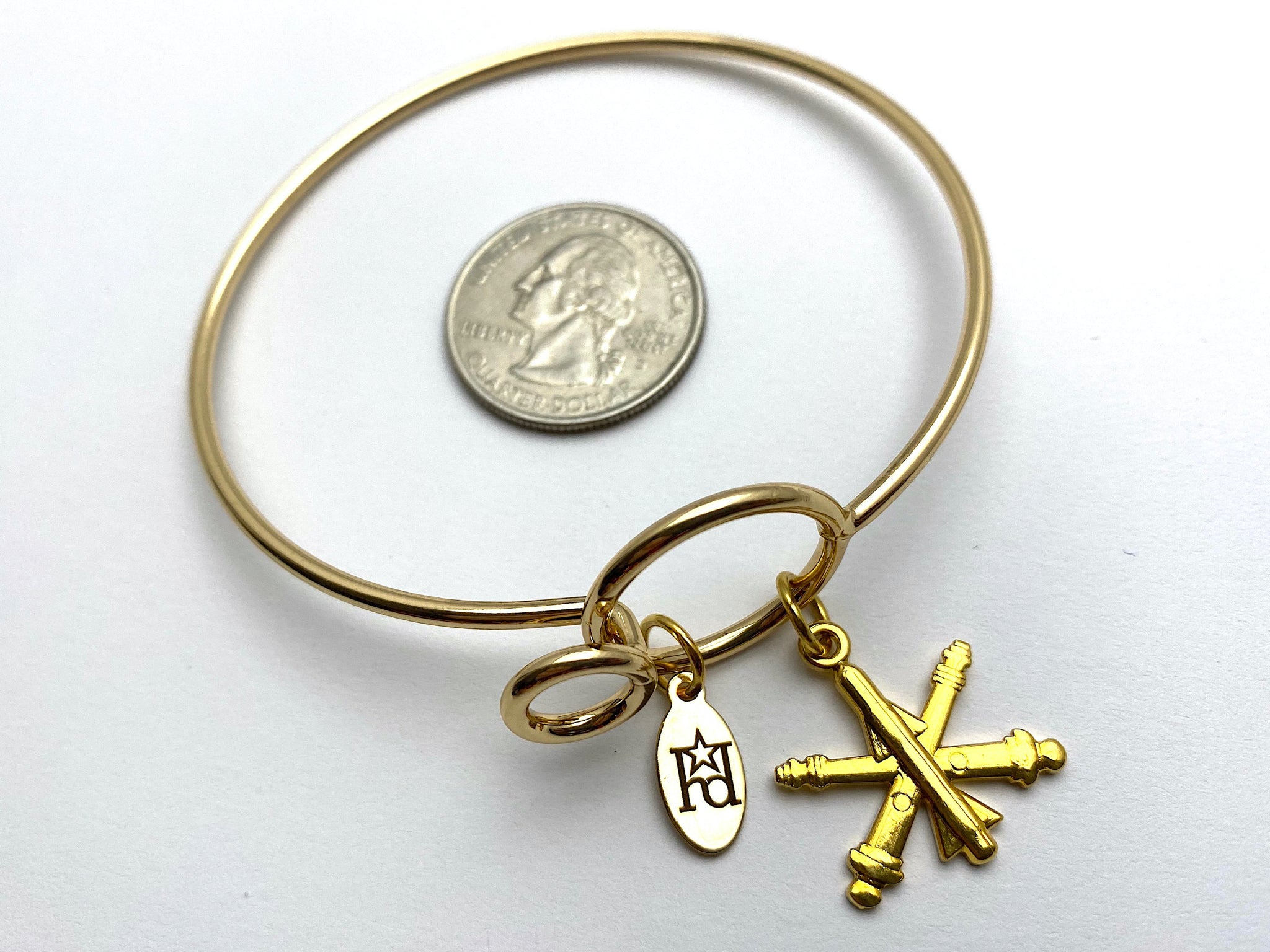 A gold-colored wire bracelet with the US Army Air Defense Artillery branch insignia.