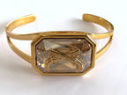 Gold cuff bracelet with a Swarovski crystal and crossed pistols insignia.