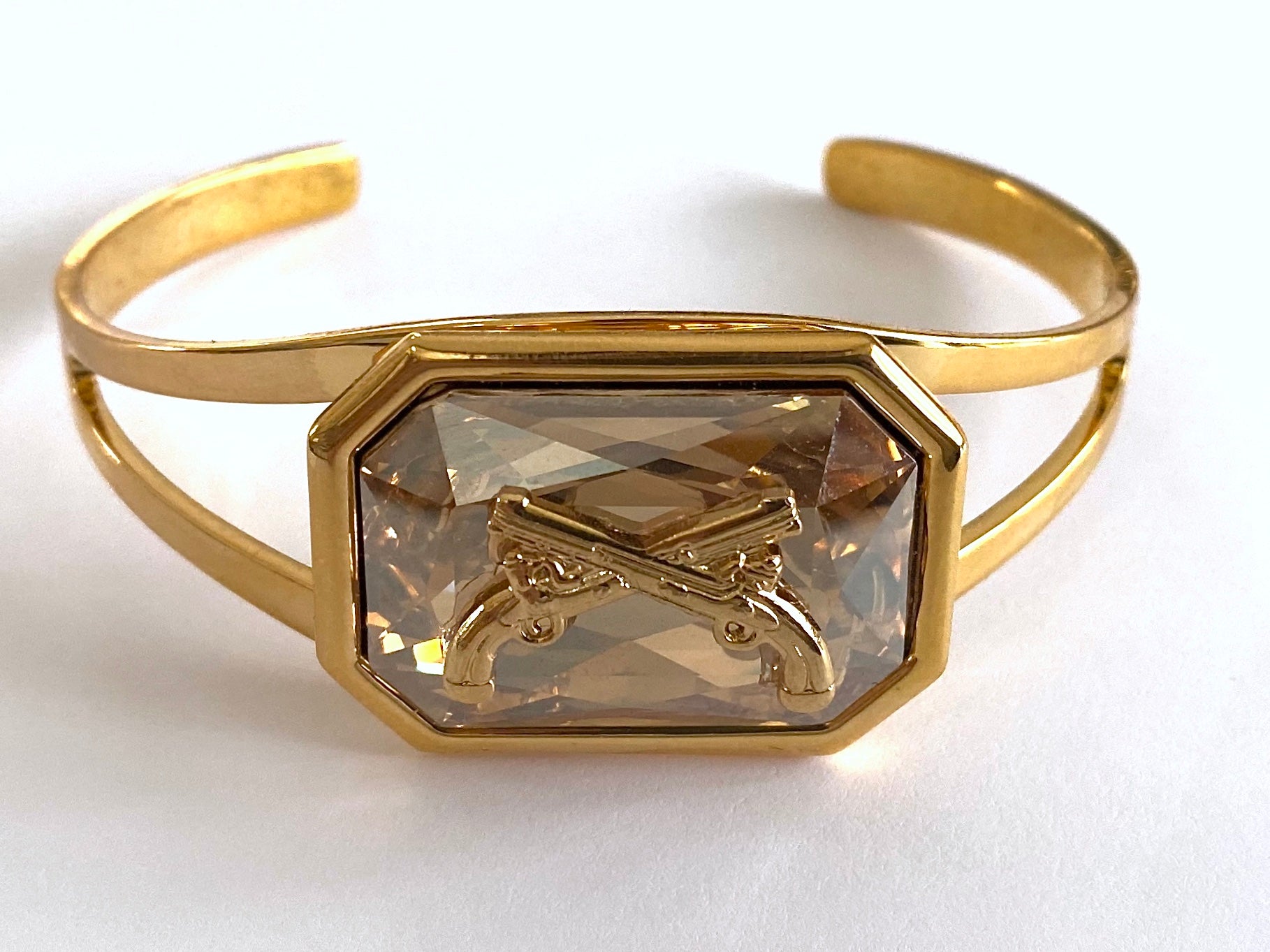 Gold cuff bracelet with a Swarovski crystal and crossed pistols insignia.