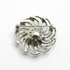 A silver-toned metal brooch with a decorative, swirling petal-like cutout design and a pin bar, shown on a plain white background.