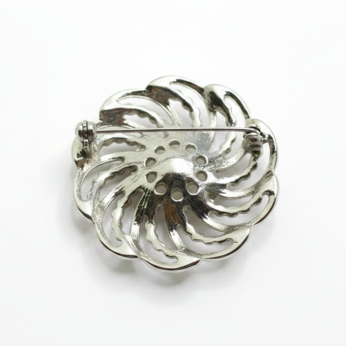 A silver-toned metal brooch with a decorative, swirling petal-like cutout design and a pin bar, shown on a plain white background.