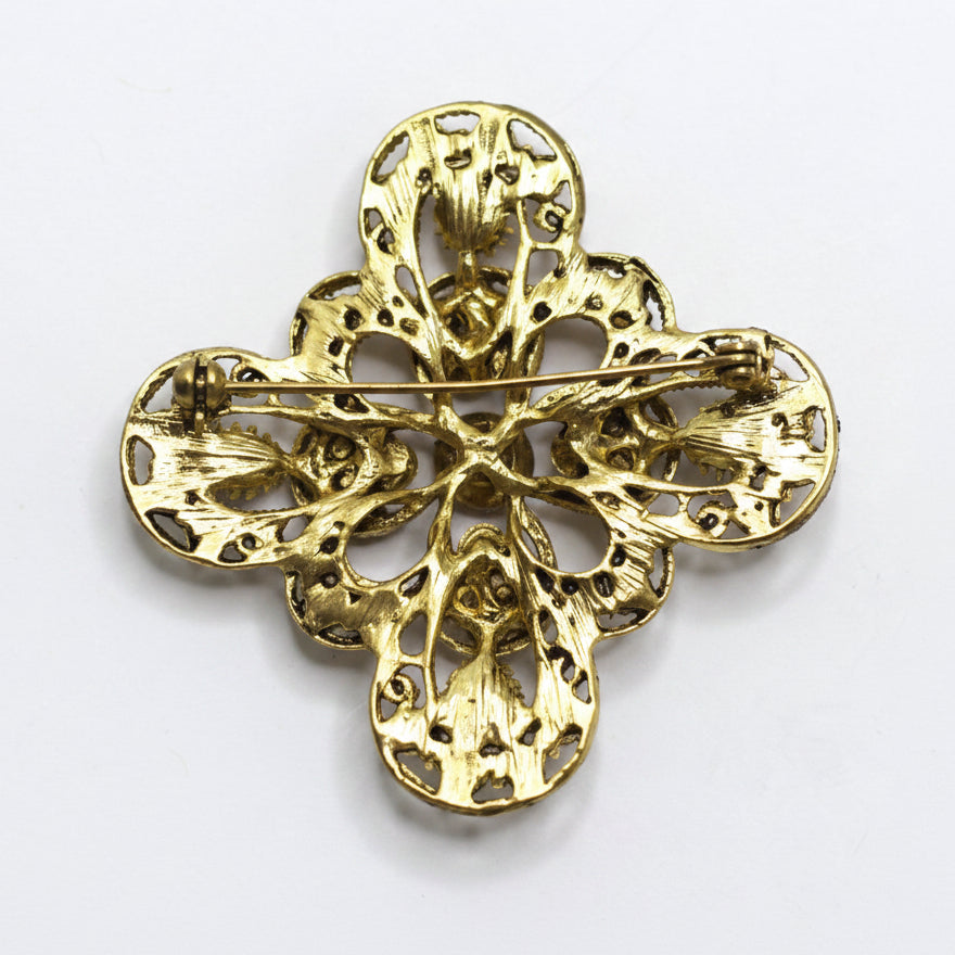 A vintage gold-tone filigree cross brooch with a pin back, displayed on a clean white background.