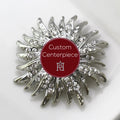 A silver brooch with clear crystals designed as a 15N pattern, featuring a custom red centerpiece with white lettering.