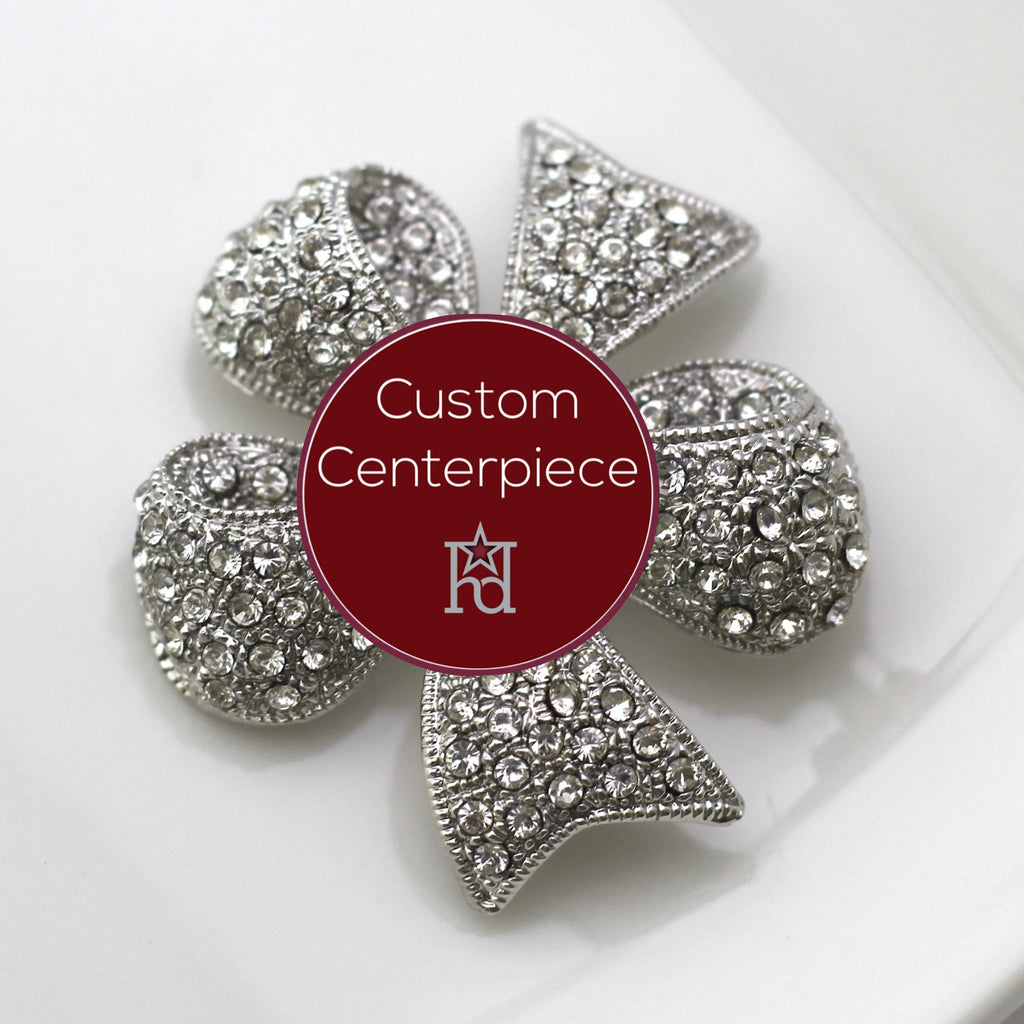 A silver brooch with clear crystals designed as a flower, featuring a central emblem, on a white plate.