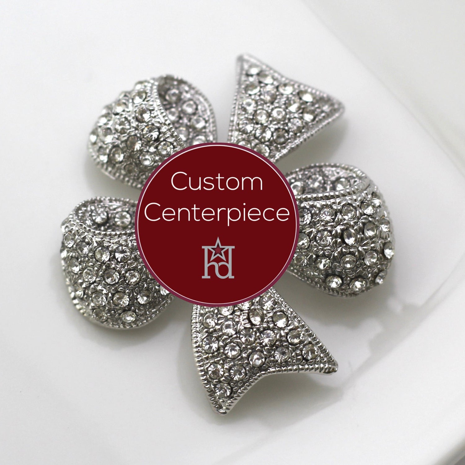 A silver brooch with clear crystals designed as a flower, featuring a central emblem, on a white plate.