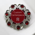 A round silver brooch with red crystals arranged in a pattern around a custom centerpiece.