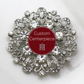 A silver brooch with clear crystals designed in a floral pattern, featuring a custom center piece with the text 'Custom Centerpiece' and the Hope Design logo.