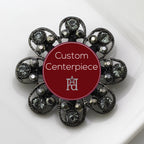 A silver brooch with black and grey crystals, featuring a circular design with a central label stating 'Custom Centerpiece' and the Hope Design logo.