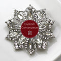 A silver brooch with clear crystals designed in a floral pattern with a custom center centerpiece.
