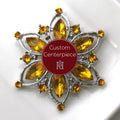 A custom-designed brooch with a silver base and citrine crystals, featuring a flower-like shape with a central larger citrine crystal surrounded by smaller ones, on a white background with a red 'H' logo in the corner.