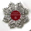 A silver brooch with clear crystals designed in a floral pattern, featuring a central red label with the text 'Custom Centerpiece'.