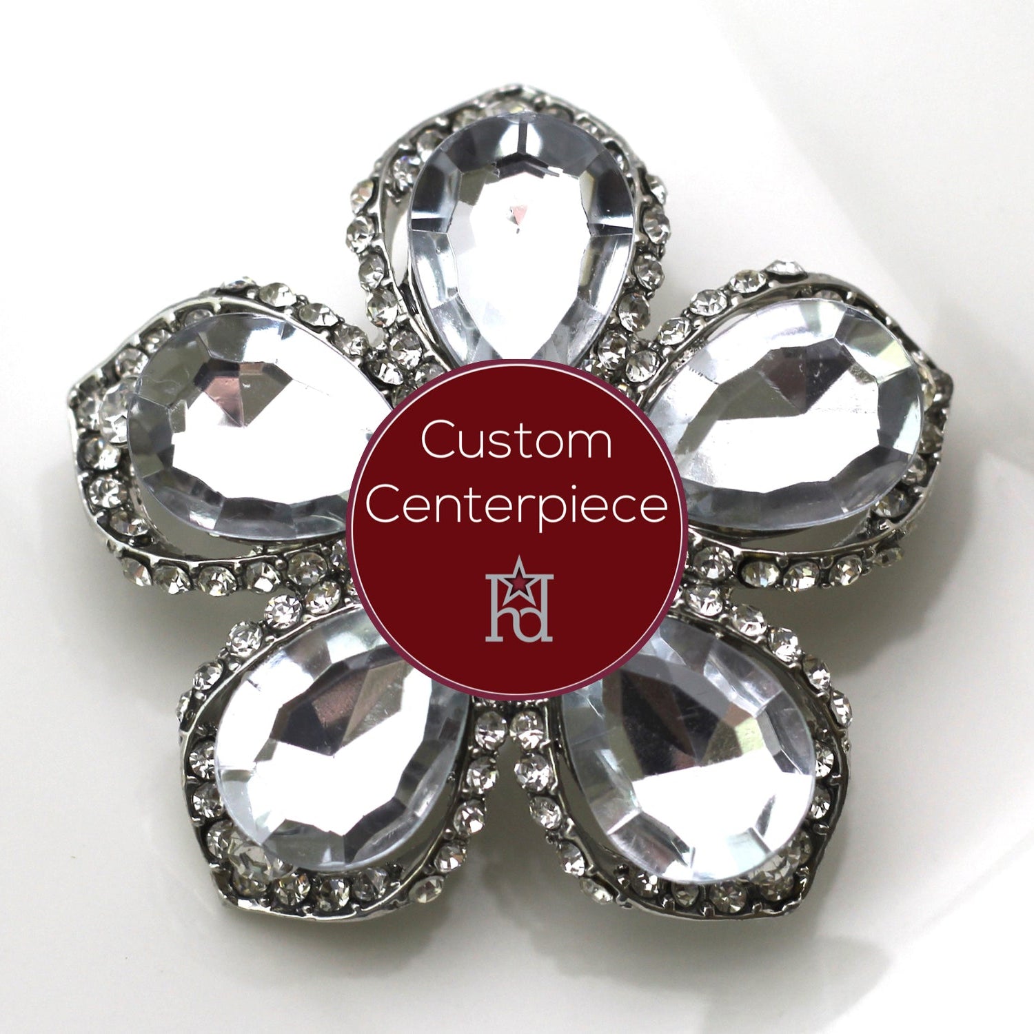A custom-designed brooch with silver and clear crystals, featuring a floral pattern and a central 23K insignia emblem.