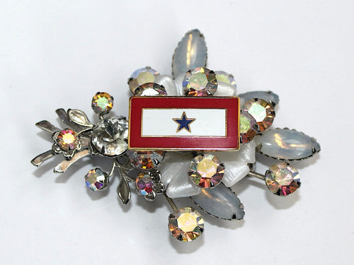 Vintage brooch with a blue star and red background, encircled by clear crystals and silver-colored metal accents.