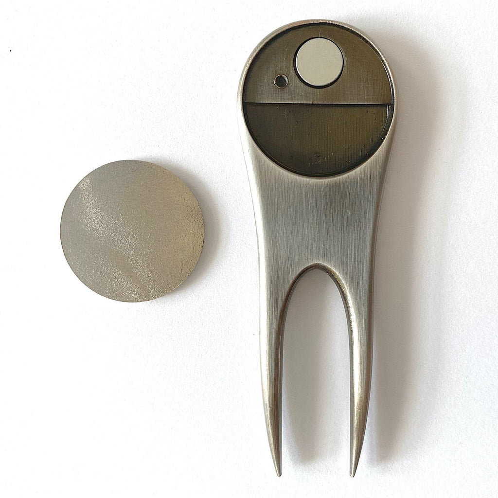 Metallic golf divot tool and ball on a white background