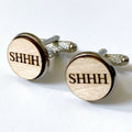 A pair of wooden cufflinks with the engraved text 'SHHH' on a round, polished surface.