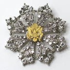 A silver brooch featuring a central eagle motif surrounded by crystal rhinestones, with a patriotic theme.