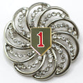 A silver brooch featuring a U.S. Army 1st Infantry Division insignia with diamond-like crystals set in a circular pattern.