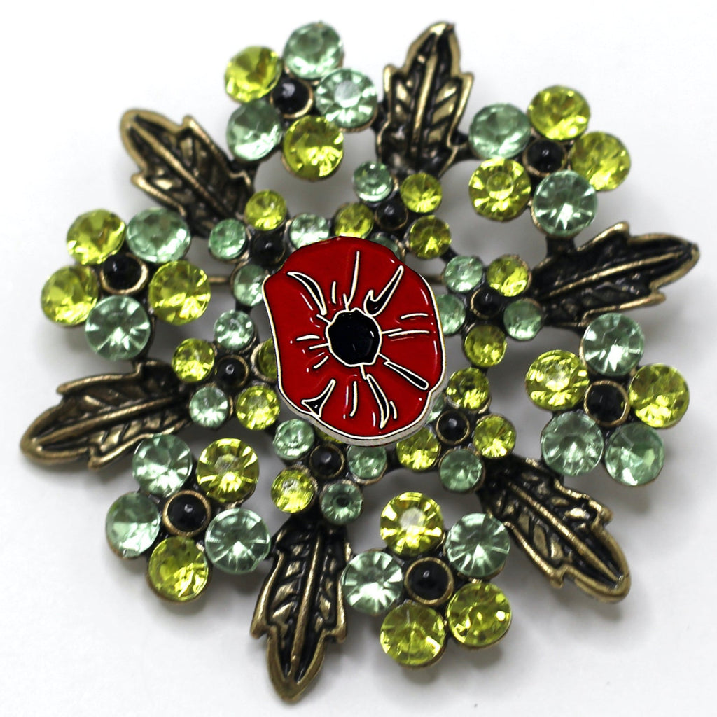 A brooch with a red poppy flower centerpiece surrounded by green and silver accents