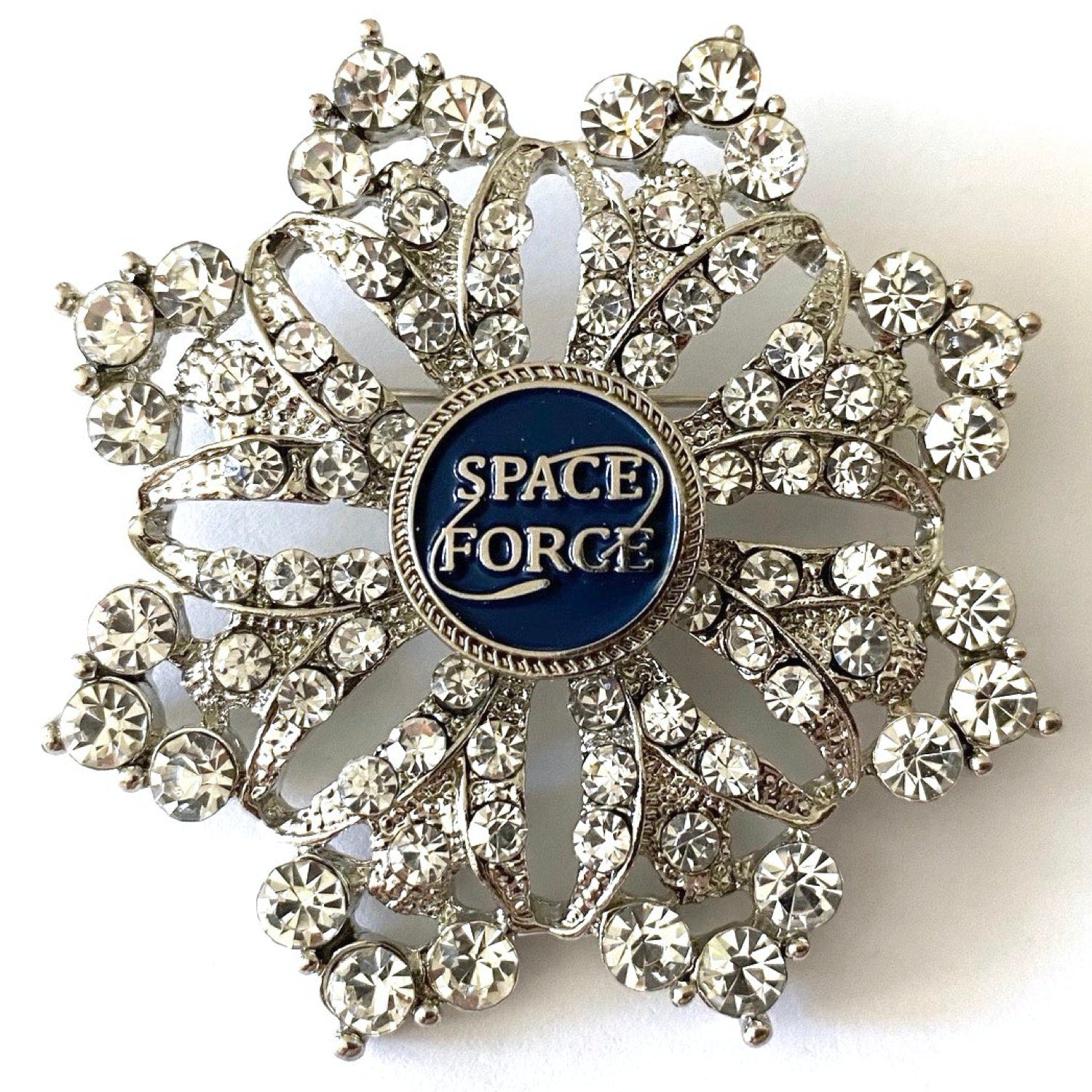 A brooch with a central Space Force emblem surrounded by crystal rhinestones on a shield-shaped background.