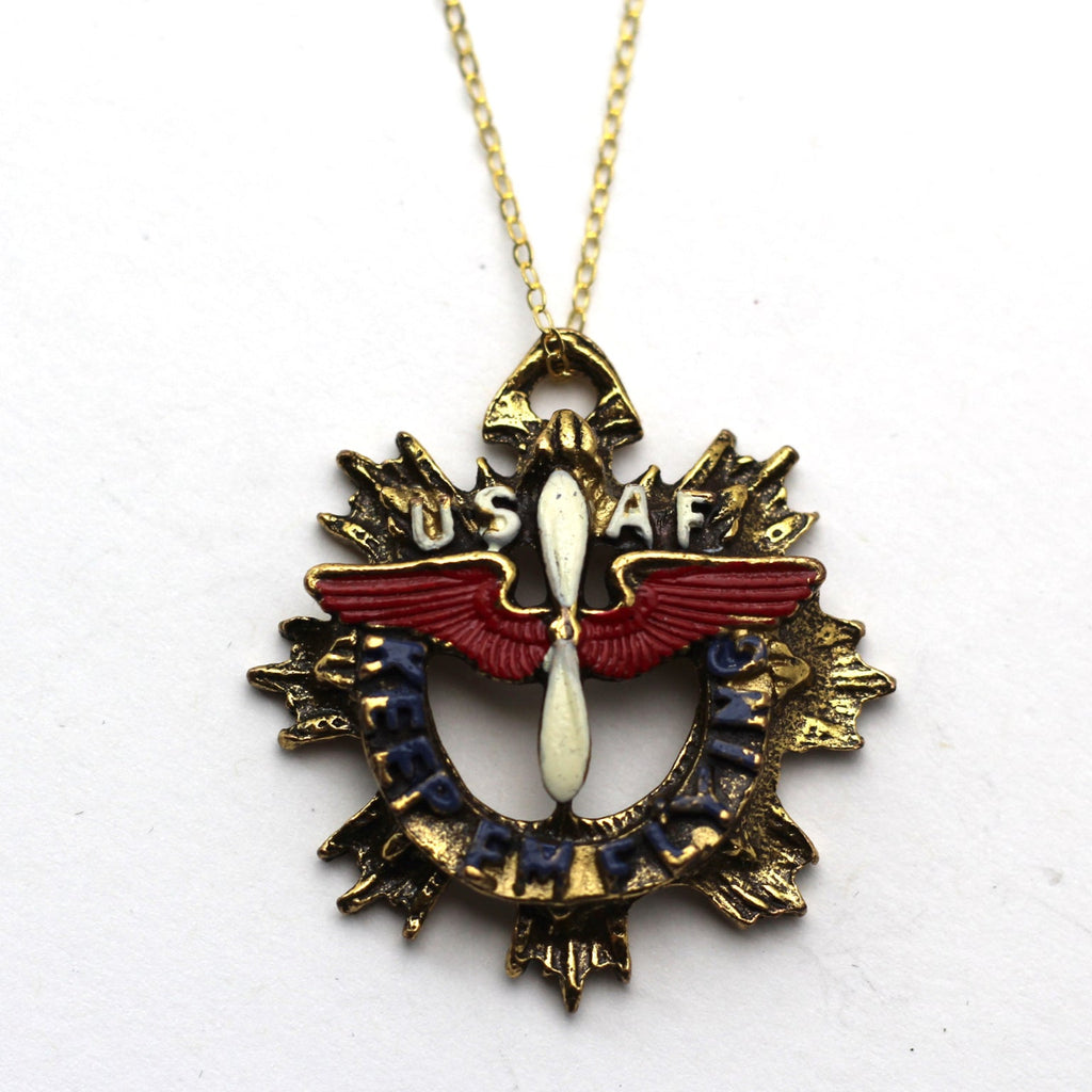 A vintage WWII-era sweetheart necklace with a gold-filled chain and a red, blue, and gold colored pendant featuring an aviation 'keep em flying' charm, and the USAF logo.