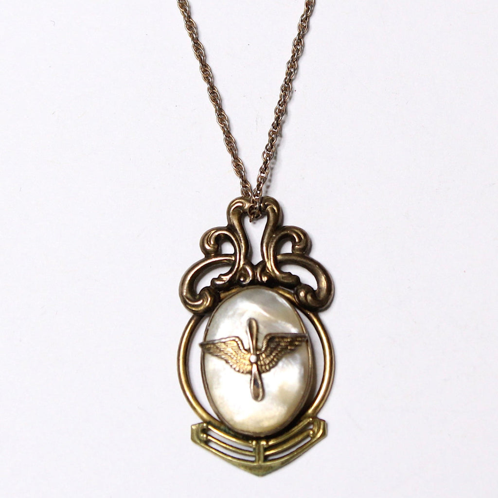 A vintage gold-filled necklace with a mother of pearl pendant featuring an aviation 'prop and wings' insignia, on a chain.