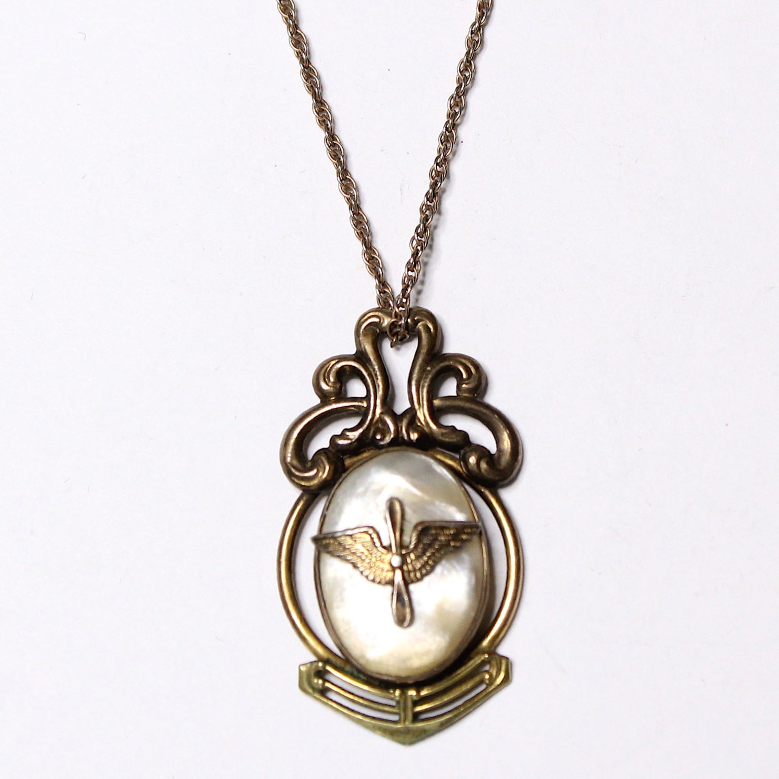 A vintage gold-filled necklace with a mother of pearl pendant featuring an aviation 'prop and wings' insignia, on a chain.