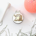 Golf ball marker with dolphin design on a white surface with grass and a pink golf ball.